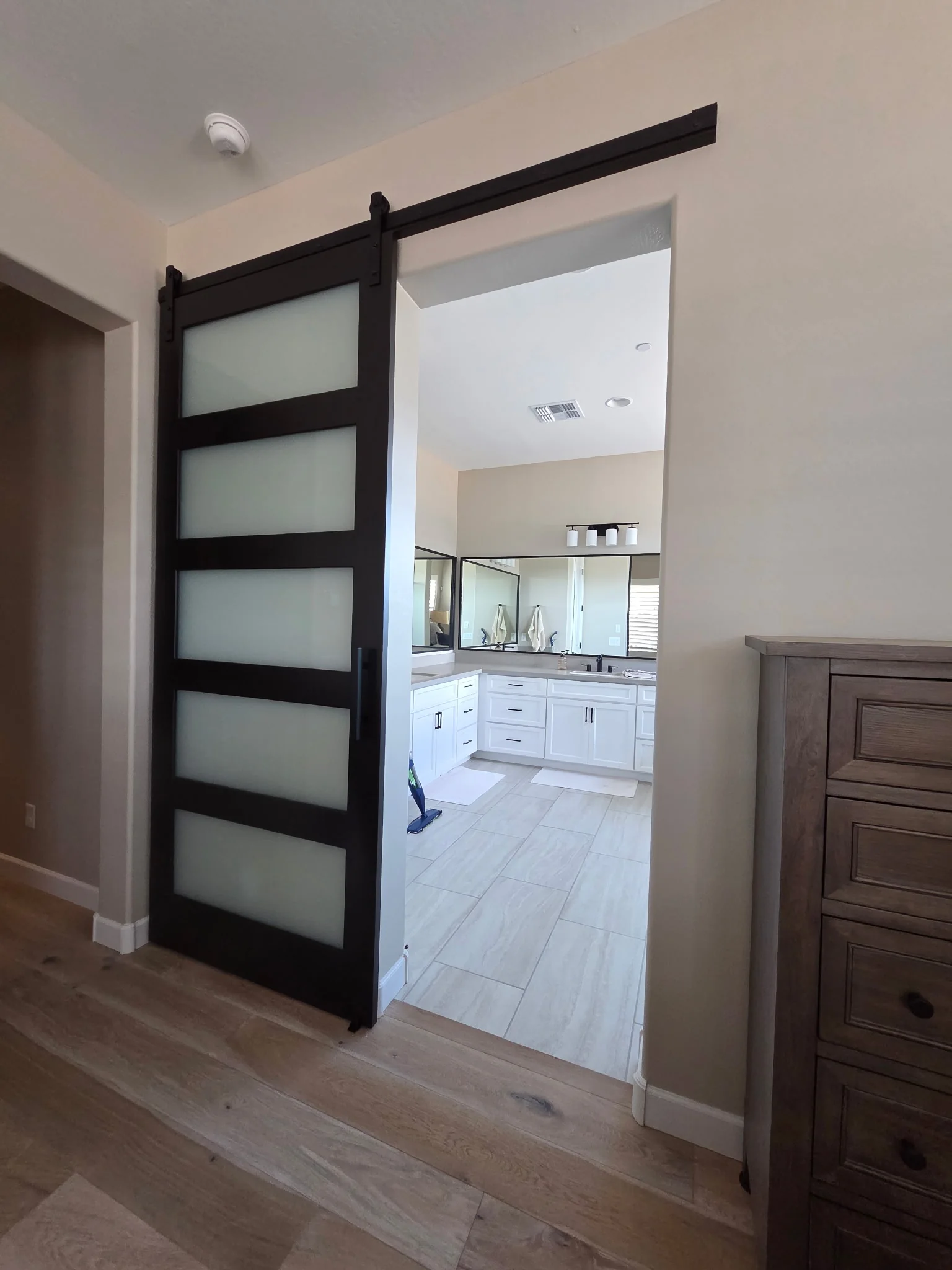 Five-Lite Frosted Glass barn door, a dark single sliding leaf with five stacked horizontal glass lites, partly open at a bathroom entrance on an exposed black rail