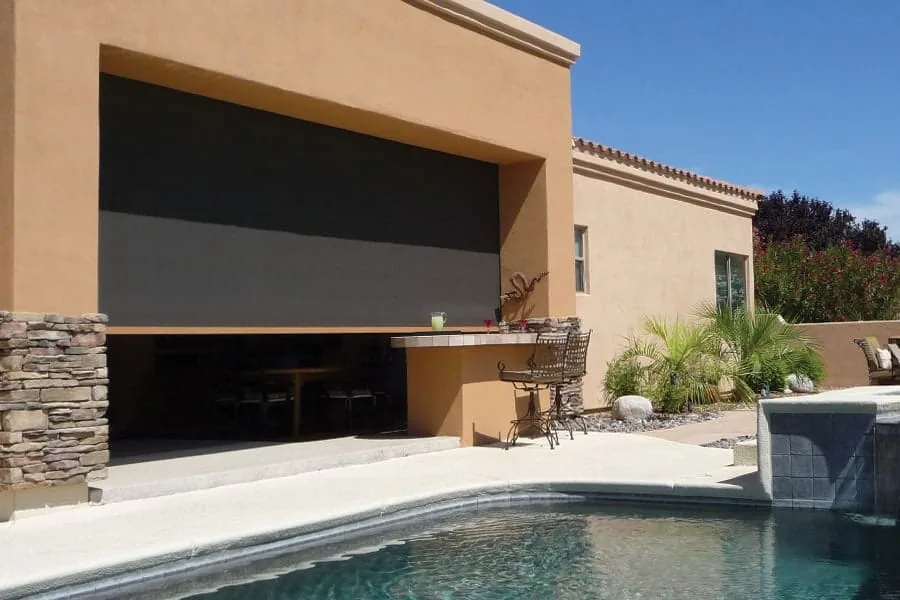 Outdoor Kitchen Shade, a solar shade lowered over an outdoor bar and kitchen opening beside a pool and spa