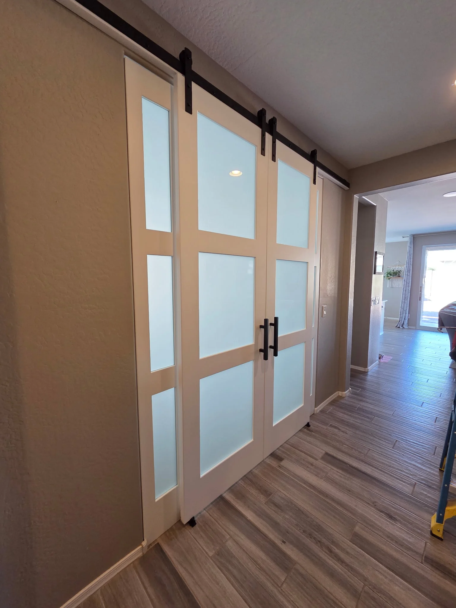 Three-Lite Frosted Glass double barn doors, white leaves with three stacked glass lites per door and exposed black sliding hardware, shown closed