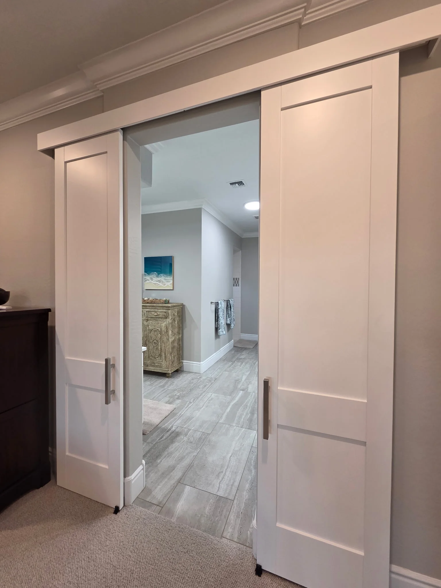 Two Panel Double Slider barn doors, white Shaker-style leaves with brushed-metal-colored pulls and a concealed track, opened apart at an ensuite bathroom