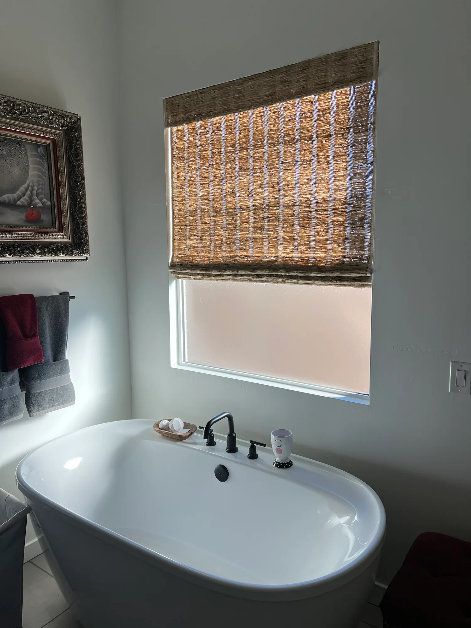Woven Wood Roman shade above a white freestanding bathtub with dark fixtures.