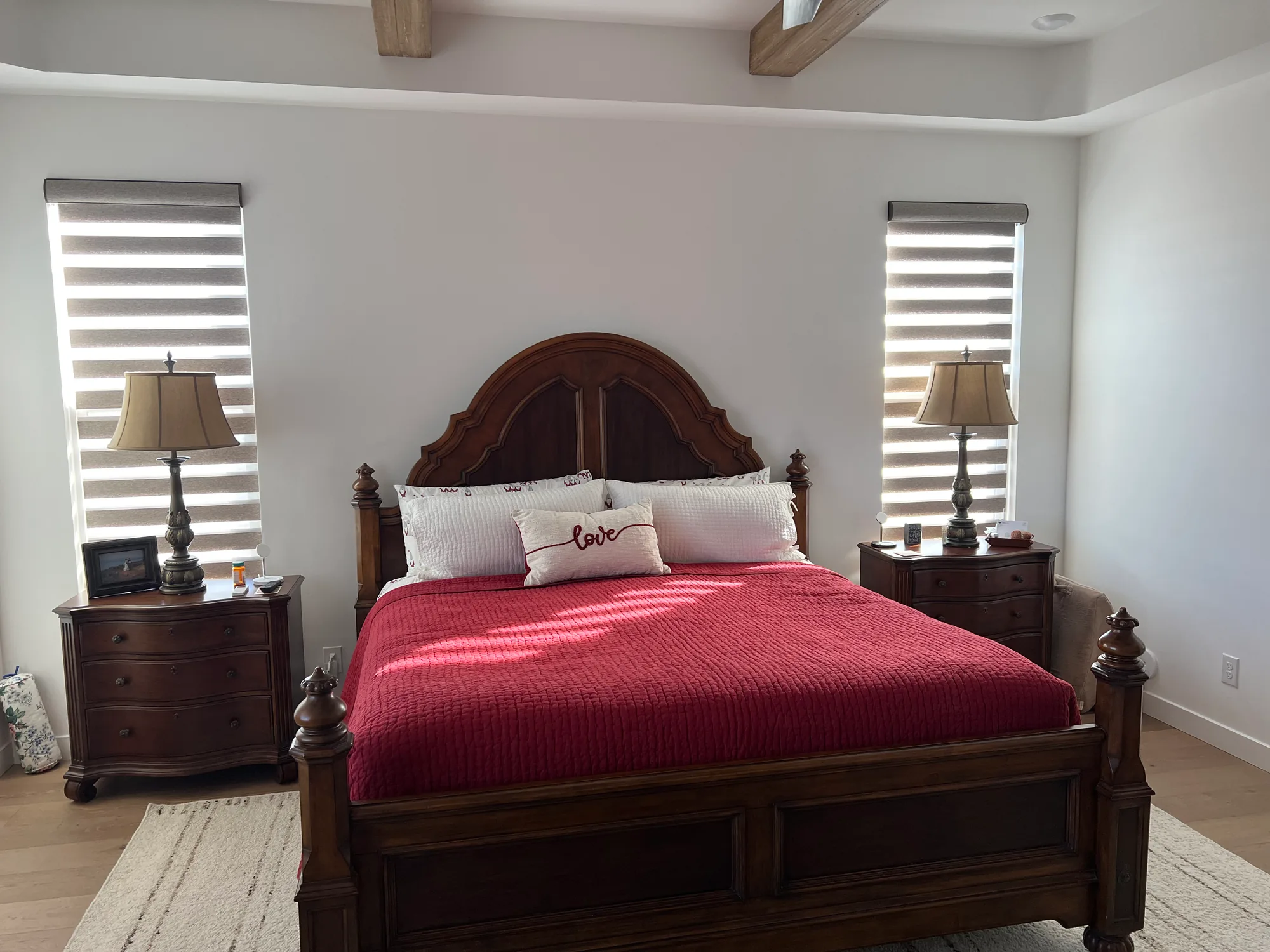 Zebra shades on two tall bedroom windows flanking a bed with a red bedspread.